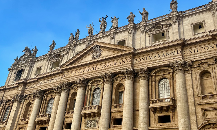 Facade of St. Peter’s Basilica in Vatican City, featuring grand columns, statues of apostles on the roofline, and Latin inscriptions across the front.