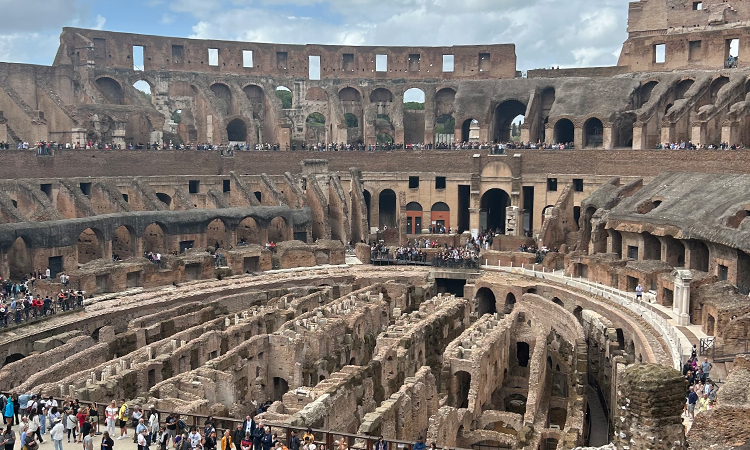 Interior view of the Colosseum in Rome, showing ancient stone walls, underground chambers, and crowds of visitors exploring the historic amphitheater.