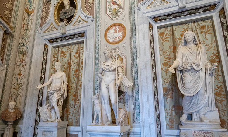 Classical marble statues displayed inside the Borghese Gallery in Rome, set against ornately decorated walls with floral patterns.