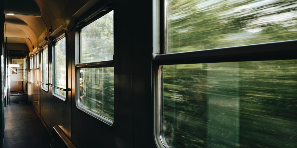 View from inside a moving train, showing blurred green scenery outside the windows and an empty corridor inside.