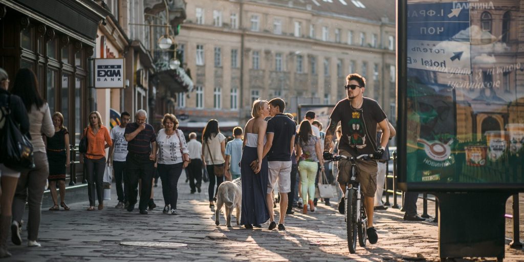 Traveler riding a bike on a European city street with pedestrians during fall season, symbolizing sustainable city transport.