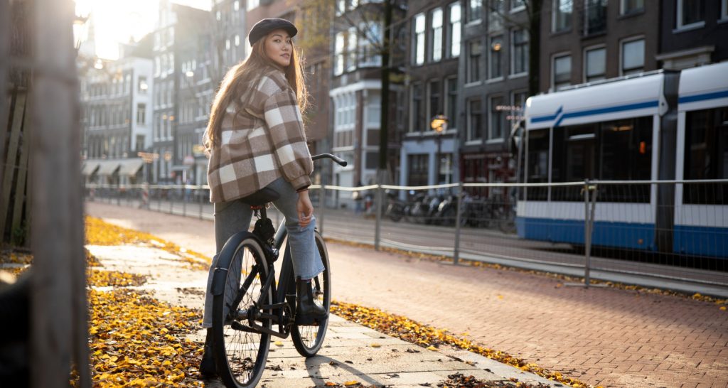 Woman cycling in Amsterdam during autumn with a tram passing by in the background.