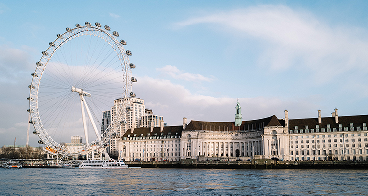 The London Eye Ferris wheel on the River Thames, with historic buildings along the waterfront.