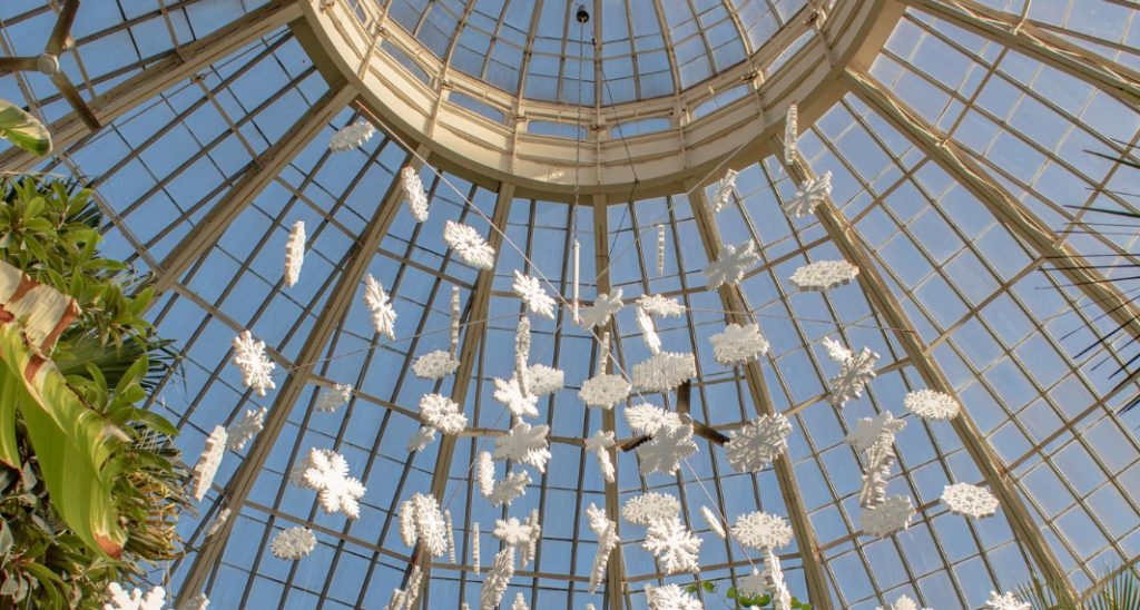 Glass dome ceiling at Kew Gardens in London, with hanging white floral sculptures and natural light streaming through the structure.